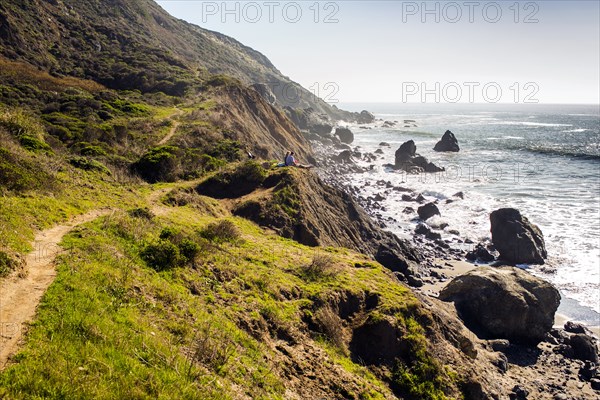 People sitting on rocky coastline trail near ocean