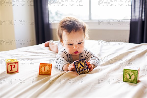Caucasian baby girl playing with blocks on bed