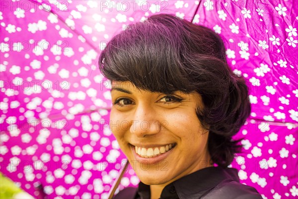 Smiling Hispanic woman holding pink umbrella