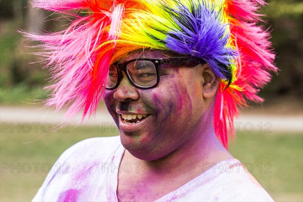 Smiling man covered in pigment powder wearing multicolor wig