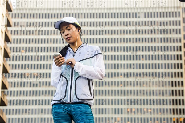 Asian runner using cell phone near highrise building