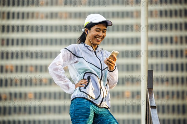 Asian runner using cell phone near highrise building