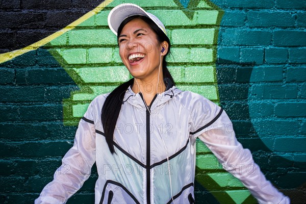 Asian runner standing near graffiti wall