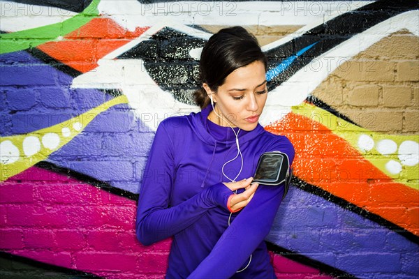 Hispanic runner using cell phone near graffiti wall