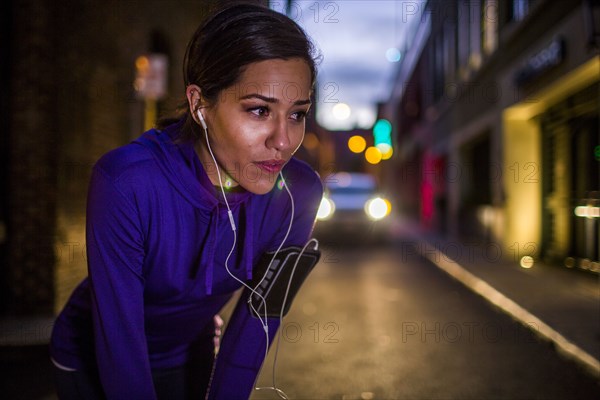 Hispanic runner resting on city street at night