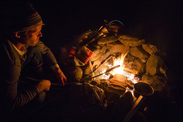 Caucasian man roasting food over campfire