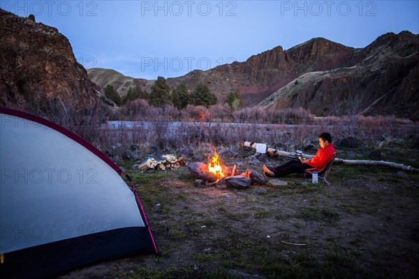 Caucasian hiker sitting near campfire in desert field