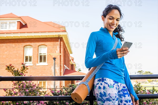 Hispanic woman with yoga mat using cell phone