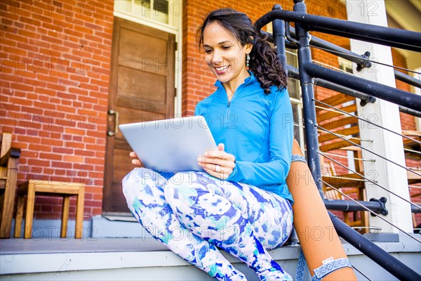 Hispanic woman using digital tablet on porch