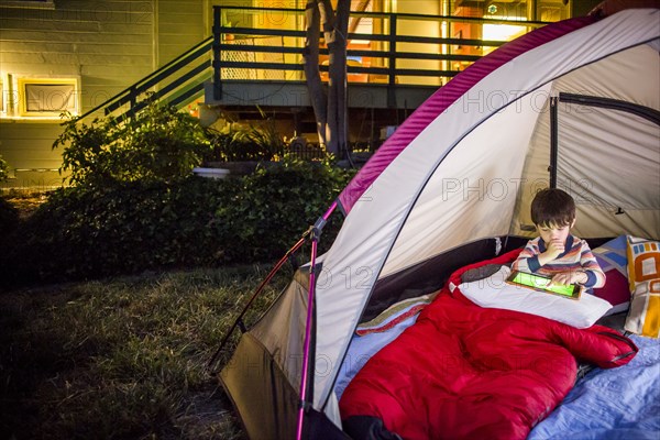 Mixed race boy using digital tablet in backyard tent