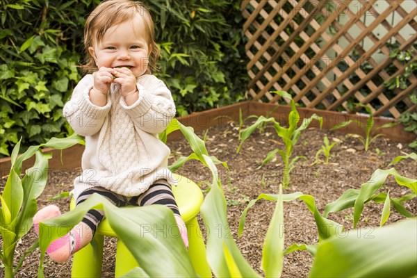 Caucasian baby girl sitting on stool in vegetable garden