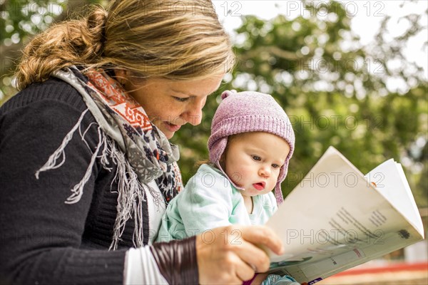 Caucasian mother and baby daughter reading in park