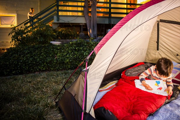 Mother watching Mixed race son coloring in backyard tent