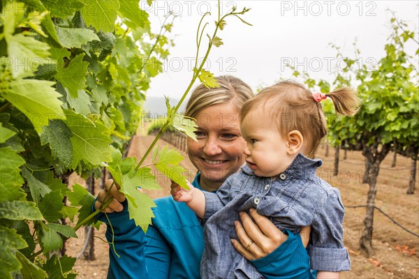 Caucasian mother and daughter admiring vine in vineyard