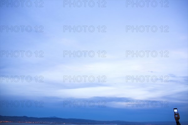 Hand holding cell phone under twilight sky