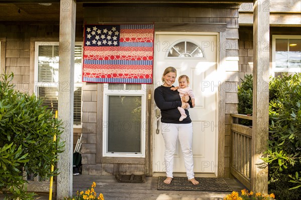 Caucasian mother holding baby daughter on front porch