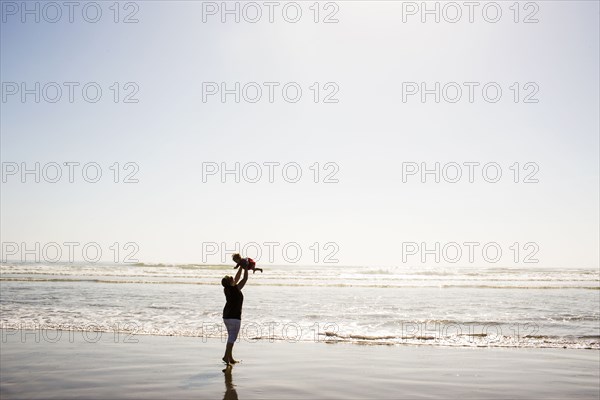 Caucasian mother lifting baby daughter on beach