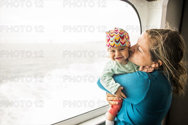 Caucasian mother kissing baby daughter at window