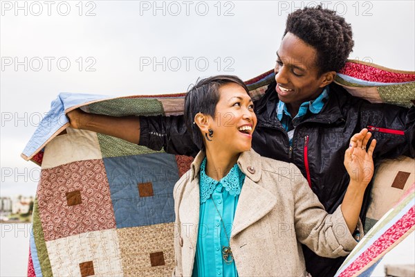 Couple wrapping themselves in blanket outdoors