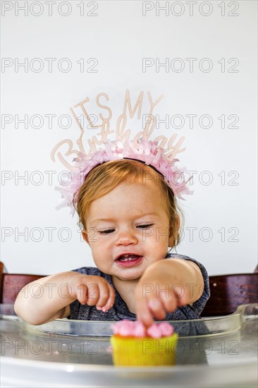 Caucasian baby girl eating birthday cupcake