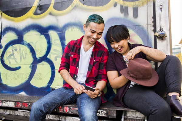 Friends using cell phone on graffiti truck