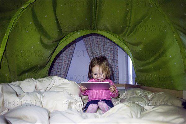 Caucasian baby girl using digital tablet in tent