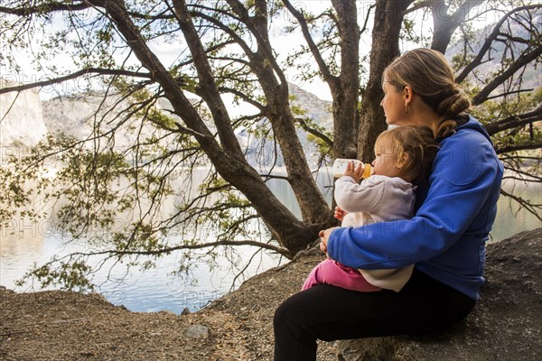 Caucasian mother and daughter sitting at lake