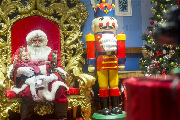 Caucasian girl sitting on lap of Santa and crying