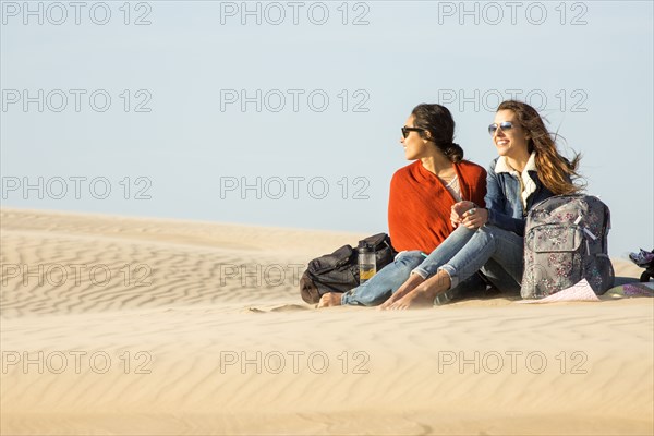 Mixed race women sitting in sand dunes