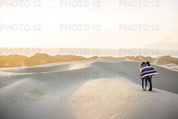 Mixed race women wrapped in blanket in sand dunes