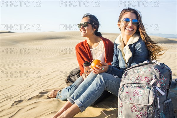 Mixed race women sitting on sand dunes