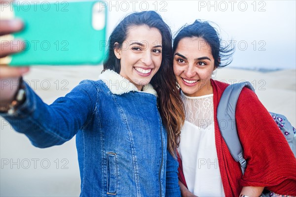 Mixed race women taking selfie on beach