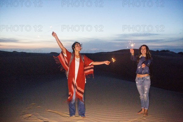 Mixed race women playing with sparklers on sand dunes