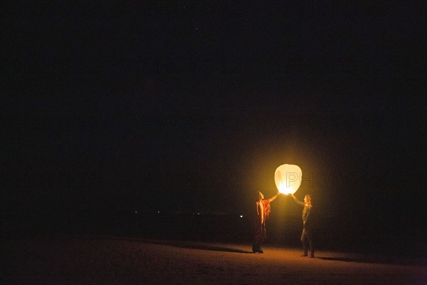 Mixed race women flying lantern at night
