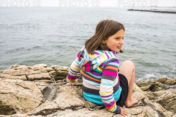 Smiling Caucasian girl sitting on rocks at ocean