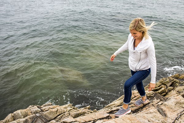 Caucasian woman walking on rocks at ocean