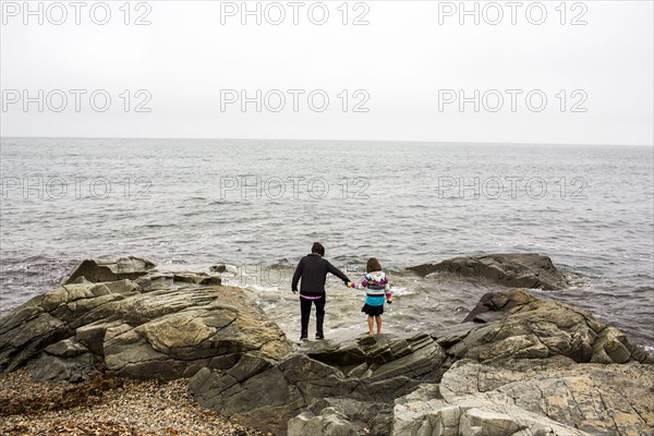 Caucasian mother and daughter holding hands on rocks at ocean