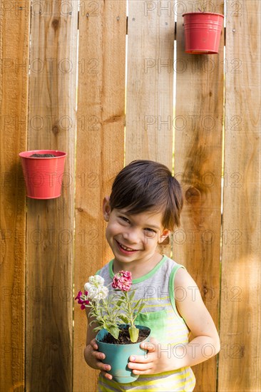 Smiling Mixed Race boy holding flowers at wooden fence