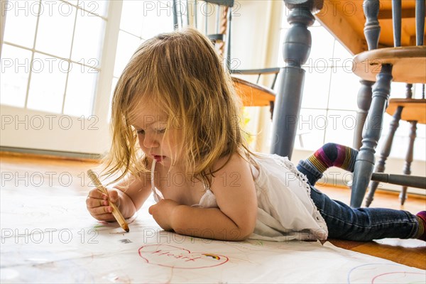 Caucasian girl laying on floor drawing on paper