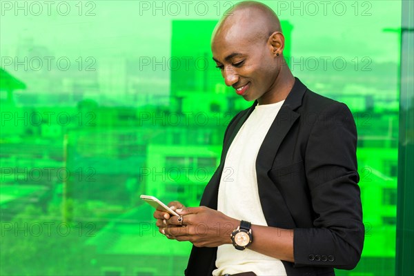 Smiling gay Black man texting near green window