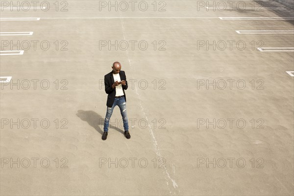 Gay Black man texting in empty parking lot