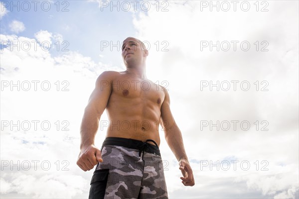 Caucasian man with bare chest standing under cloudy sky