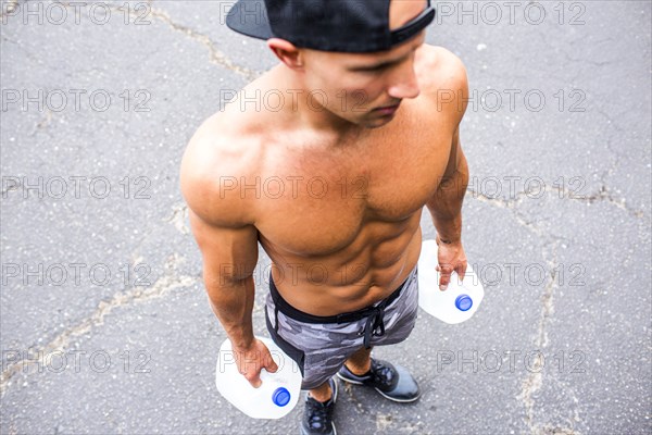 Caucasian man with bare chest holding jugs of water