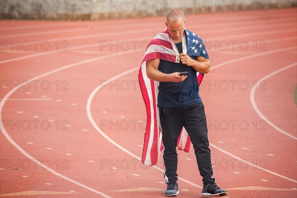 Caucasian man wearing American flag as cape on track texting on cell phone