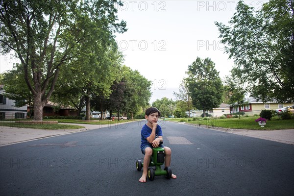 Pensive mixed race boy sitting on toy tractor in street