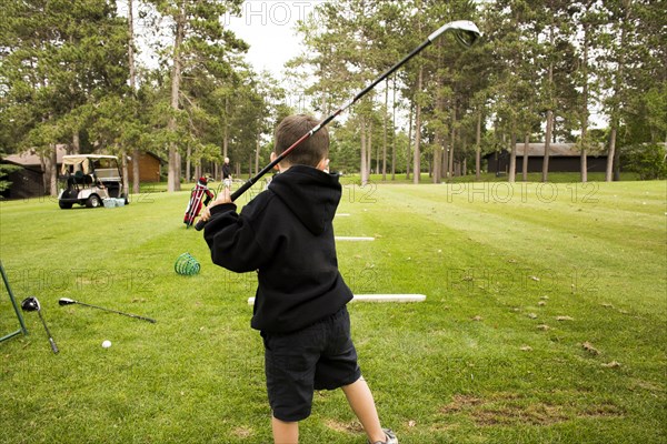 Mixed race boy swinging golf club