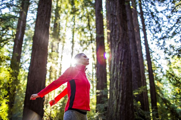 Woman stretching arms in sunny forest