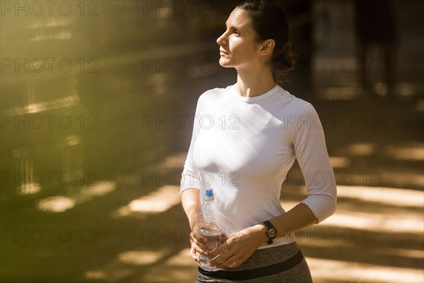 Pensive woman holding water bottle in sunny forest