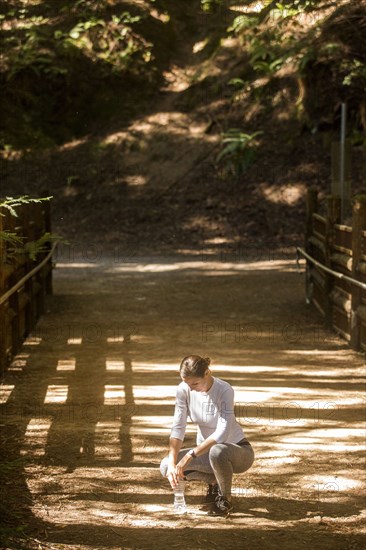 Crouching woman holding water bottle on sunny path