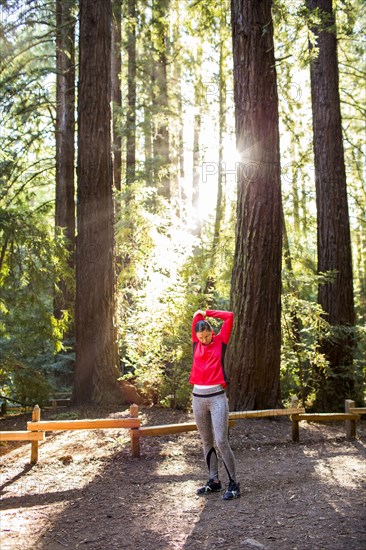 Serious woman stretching arm on forest path